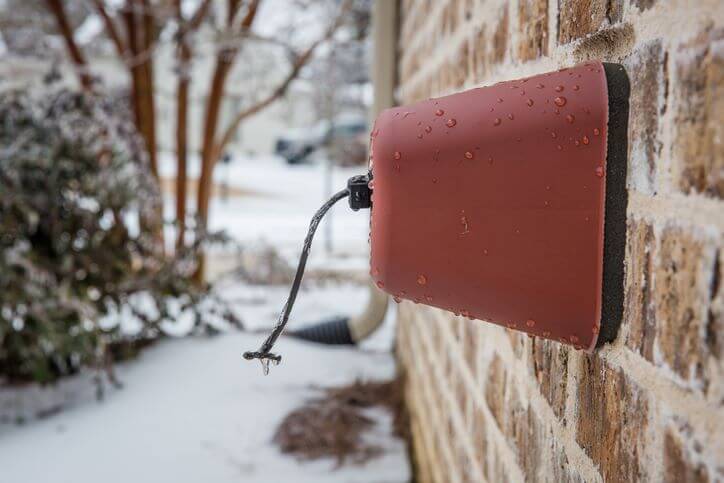 Outdoor brown spigot cover in the winter with icicles on it