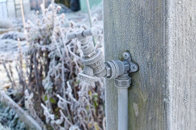 Close up of outdoor water tap covered in fros attached to a wooden post on an allotment garden in winter