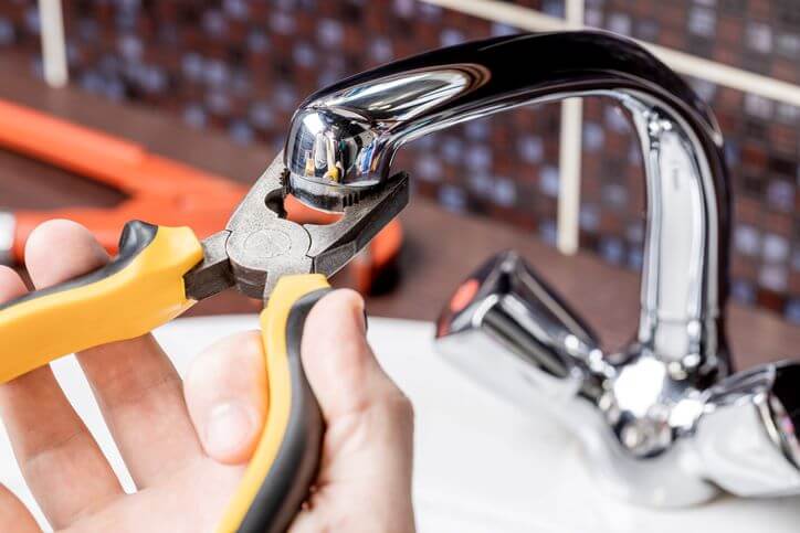 plumber using pliers to adjust leaky facet in bathroom. 